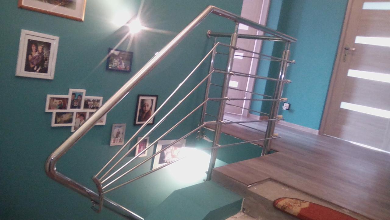 Klatka schodowa z turkusowymi ścianami udekorowanymi ramkami ze zdjęciami i nowoczesną balustradą ze stali nierdzewnej z cienkimi, poziomymi prętami.