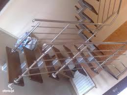 Schody z drewnianymi stopniami i nowoczesną metalową barierką z poziomymi prętami, widok z dołu, oświetlenie mieszane.