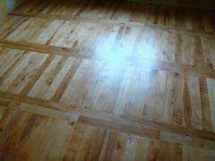 Odnowiona podłoga z jasnego drewna, z wyraźnym wzorem desek ułożonych w prostokąty, widoczne delikatne refleksy światła.