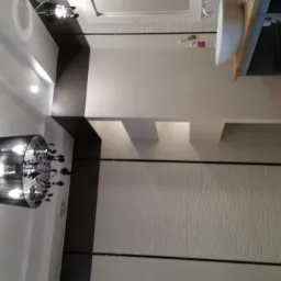 Nowoczesna łazienka z białymi płytkami o falistej strukturze, czarnymi akcentami, designerskim chromowanym żyrandolem i podwieszaną szafką umywalkową z drewnianym blatem.