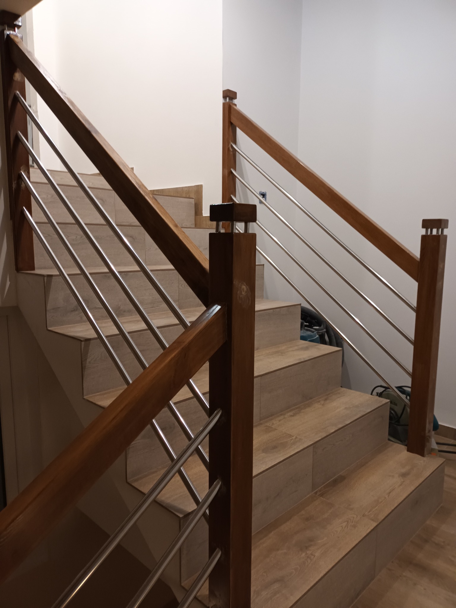 Wyłożone płytkami schody z drewnianą balustradą i metalowymi poprzeczkami, widoczne narzędzia na podeście.