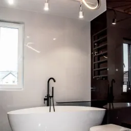 Nowoczesna łazienka z wolnostojącą wanną, czarną armaturą i designerską lampą sufitową w kształcie spirali.