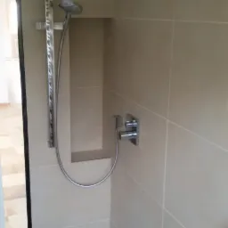 Nowoczesna kabina prysznicowa z beżowymi płytkami, deszczownicą, słuchawką prysznicową i wnęką na kosmetyki.