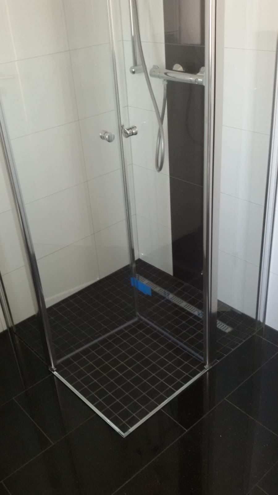 Nowoczesna kabina prysznicowa z czarną mozaiką podłogową i białymi płytkami ściennymi, widoczny chromowany zestaw prysznicowy i odpływ liniowy.