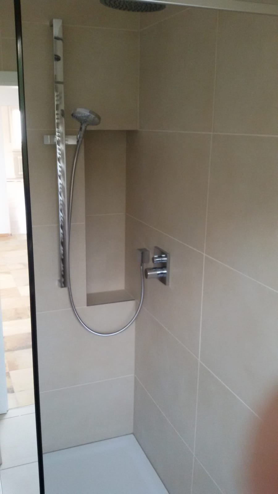 Nowoczesna kabina prysznicowa z beżowymi płytkami, deszczownicą, słuchawką prysznicową i wnęką na kosmetyki.