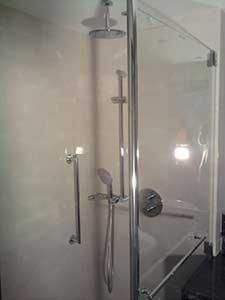 Kabina prysznicowa z deszczownicą i chromowanymi elementami wykończeniowymi, widok z boku, jasne płytki na ścianach.