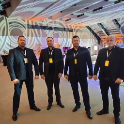 Agencja Ochrony Osób i Mienia Astrea Ochrona Imprez Masowych - Czterech ochroniarzy w czarnych garniturach stoi w eleganckim wnętrzu z dekoracjami i oświetleniem, prezentując profesjonalny wizerunek firmy ochroniarskiej.