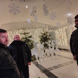 Agencja Ochrony Osób i Mienia Astrea Ochrona Imprez Masowych - Trzech ochroniarzy w czarnych kurtkach na tle świątecznej dekoracji z reniferami i choinkami, ochrona imprezy okolicznościowej.