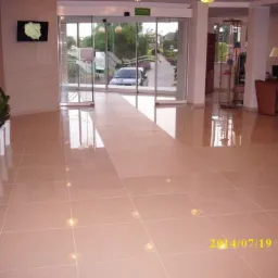 Beżowa, błyszcząca podłoga z płytek ceramicznych w holu wejściowym z wbudowanymi punktami świetlnymi, odbijająca światło z zewnątrz i elementy wyposażenia.