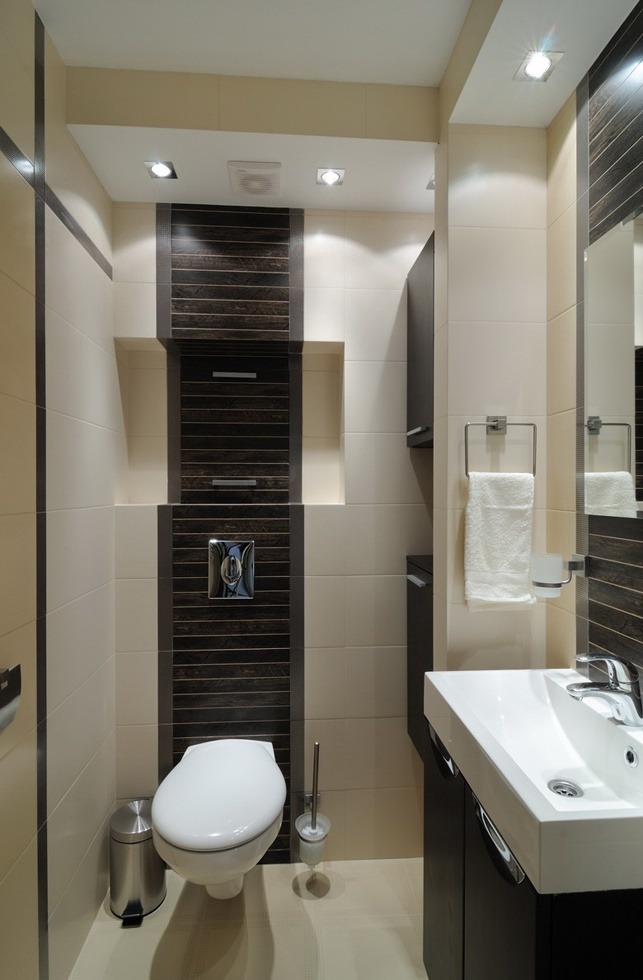 Nowoczesna łazienka z beżowo-brązowymi płytkami, podwieszaną toaletą i umywalką z szafką, oświetleniem punktowym i dekoracyjnymi wnękami.