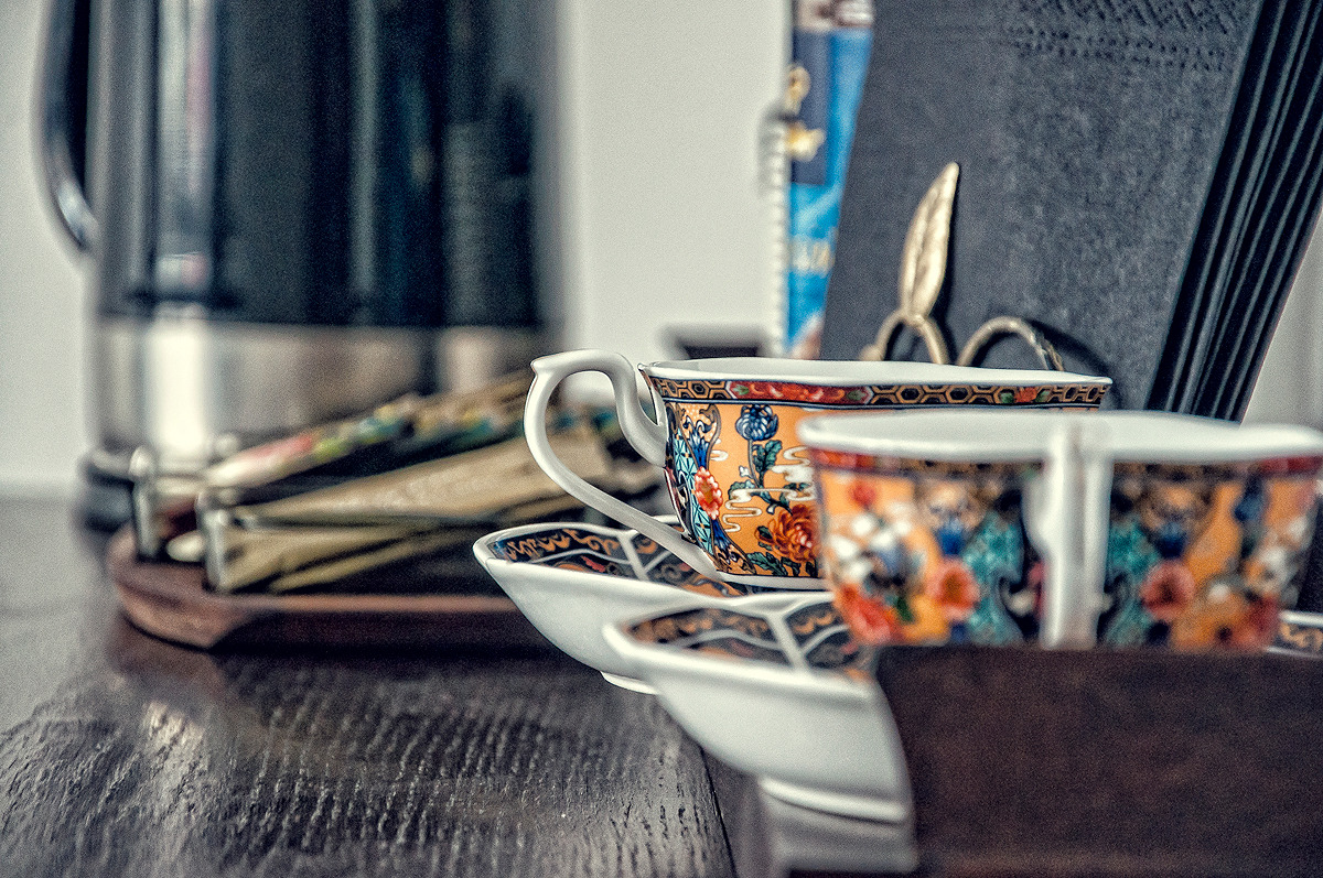 Stylowe filiżanki w orientalny wzór na ciemnym, drewnianym biurku w biurze. W tle czajnik elektryczny i inne akcesoria biurowe. Przytulna aranżacja przestrzeni biurowej.