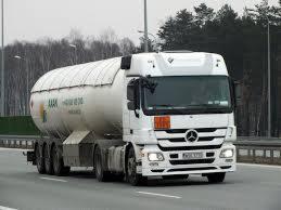 Ciężarówka cysterna z pomarańczową tablicą ostrzegawczą przewożąca paliwo, widoczna na autostradzie, w tle las.