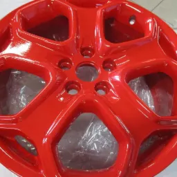 Błyszcząca, czerwona felga aluminiowa po odnowieniu, widoczna z bliska, z delikatnym odbiciem światła na powierzchni i folią ochronną w tle.