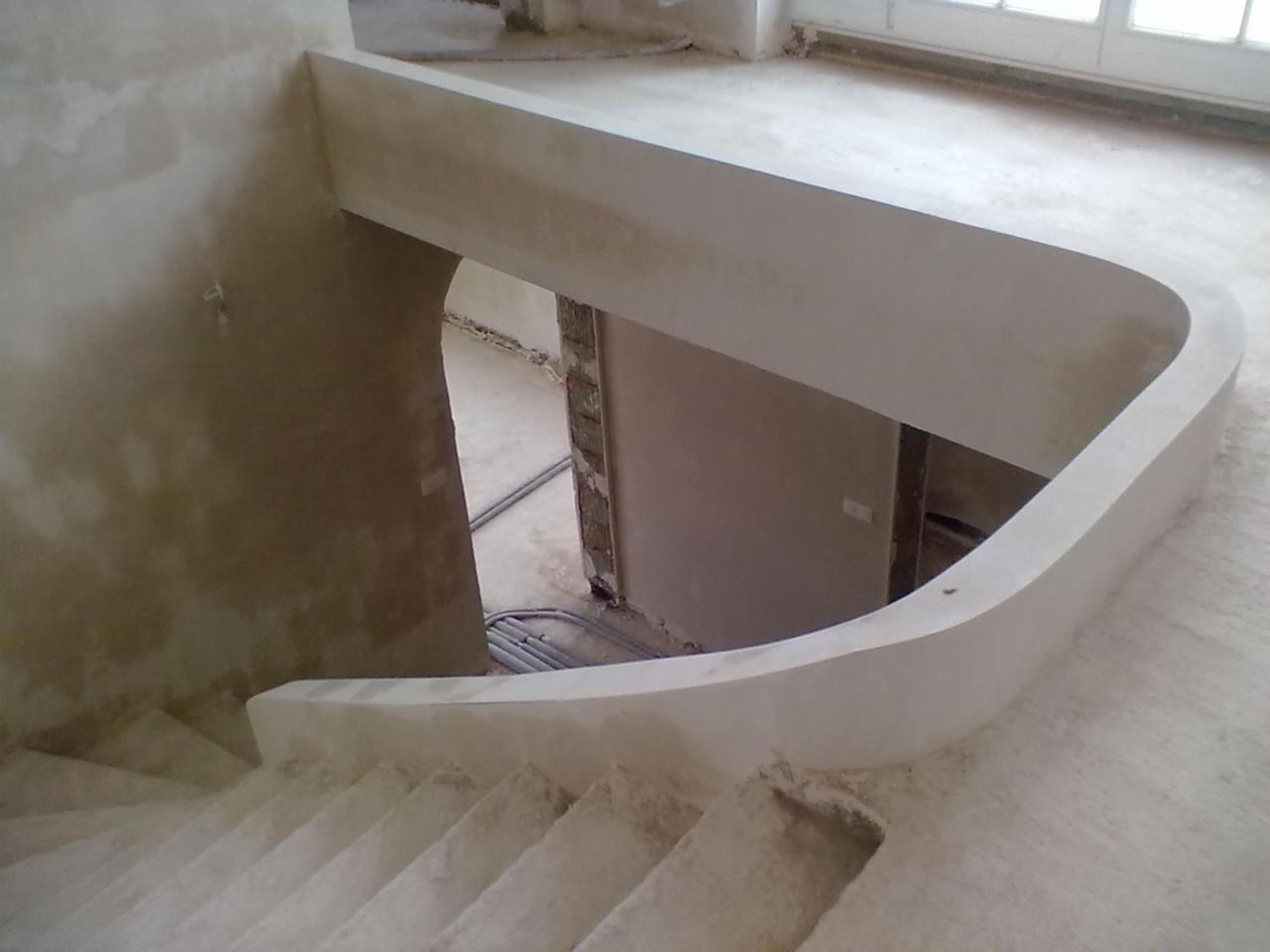 Wykończone tynkiem maszynowym schody z zaokrąglonym wejściem, widok z góry. Szare, surowe wnętrze w trakcie prac wykończeniowych.