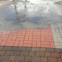 DOMI Profesjonalne mycie wysokociśnieniowe - Mokry fragment chodnika z kostki brukowej w trzech odcieniach, z odbiciem nieba w kałuży i narożnikiem ceglanego muru