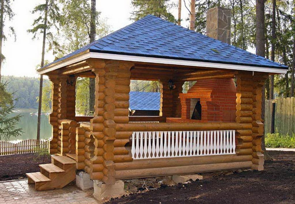 Drewniana altana z bali z murowanym grillem, niebieski dach z gontu bitumicznego, widok na jezioro w tle.
