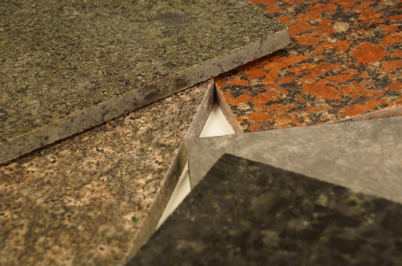 Bliski plan próbek kostki granitowej w różnych kolorach i fakturach, ułożonych warstwami, ukazujących przekrój i strukturę kamienia.