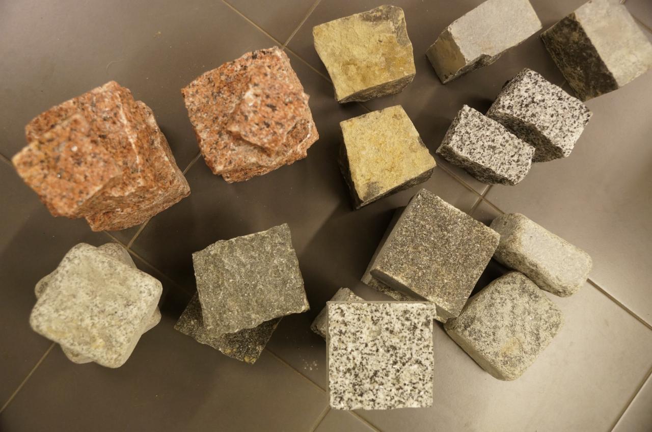 Różnokolorowa kostka granitowa w Olsztynie: czerwona, żółta, szara i nakrapiana, ułożona na podłodze z płytek. Prezentacja różnorodności wzorów i tekstur.