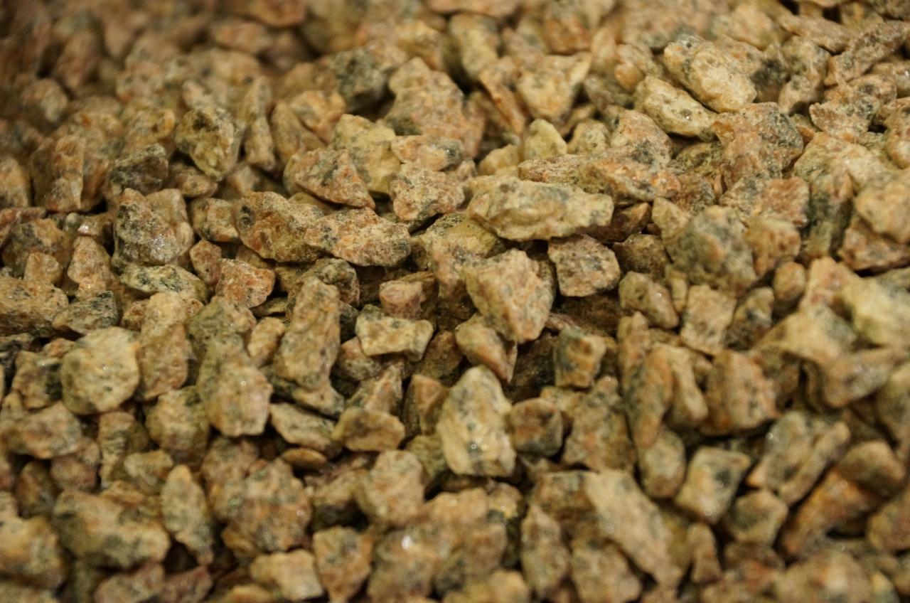 Detaliczne ujęcie brązowo-szarego grysu granitowego o nieregularnych kształtach, wypełniającego kadr. Widoczne drobne, wilgotne kamienie, faktura i zróżnicowana kolorystyka.