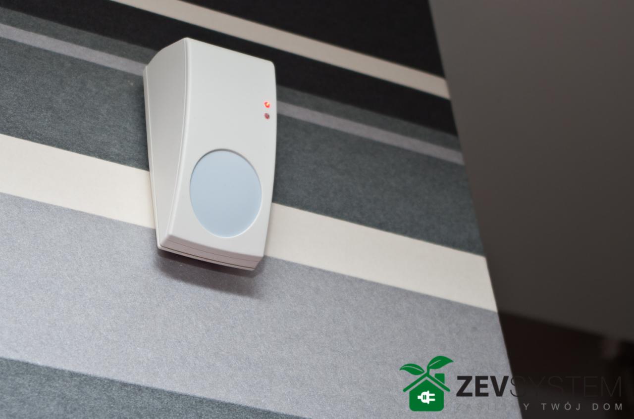 Biały czujnik ruchu systemu alarmowego Integra 64 PRO zamontowany na ścianie w paski, z widocznymi czerwonymi diodami LED.