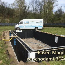 Budowa basenu Magiline ze schodami BEACH1: widok na wykop z częściowo zamontowaną konstrukcją, siatką zbrojeniową i instalacją hydrauliczną; w tle zaparkowany biały bus z reklamą firmy budującej...