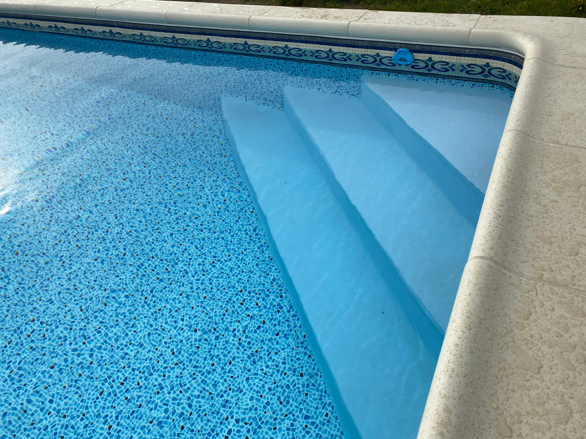 Błękitny basen z mozaikową wyściółką i trzema schodami, widoczny narożnik z kamiennym obrzeżem i dekoracyjnym pasem płytek.