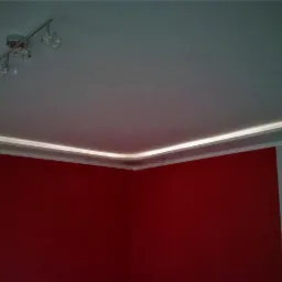 Czerwona ściana w rogu pokoju z podwieszonym sufitem z oświetleniem LED i lampą sufitową z czterema kloszami.