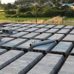 Konstrukcja stropu Teriva z pustakami i zbrojeniem, widok z góry na tle krajobrazu wiejskiego. Szary przewód wentylacyjny leży na pustakach.