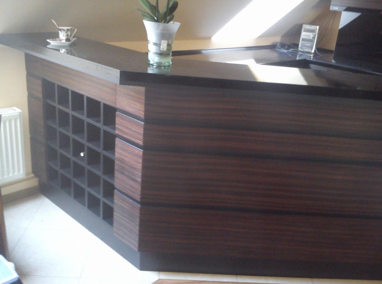 Kącik barowy z ciemnego drewna z półkami na wino, wykończony czarnym blatem, z filiżanką i kwiatem na blacie, widok z niskiego kąta.