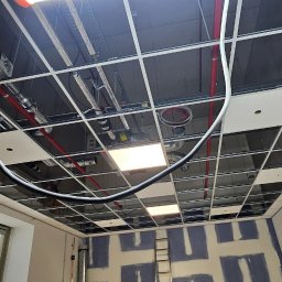 Developartus - Montaż sufitu podwieszanego kasetonowego z widocznymi instalacjami wentylacyjnymi i elektrycznymi. Ściany przygotowane do malowania, widoczna drabina.
