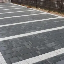 Ułożona nawierzchnia z ciemnej kostki brukowej z jasnymi pasami w Sieradzu, widok z góry na fragment posesji z ogrodzeniem.