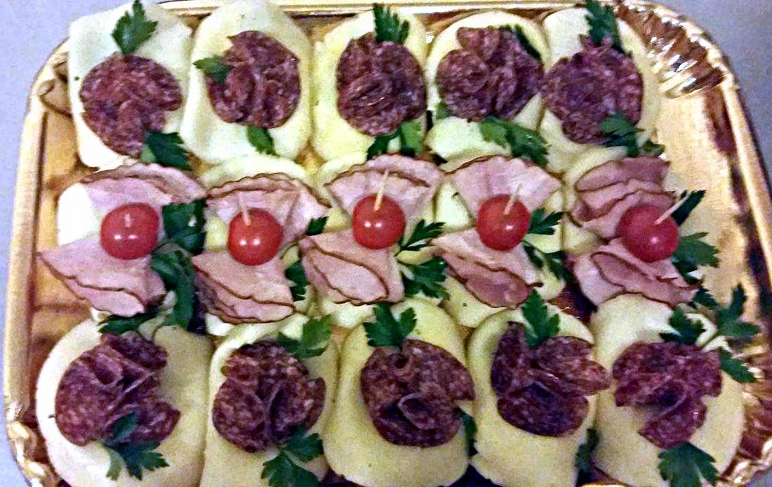 Dekoracyjne kanapeczki na złotym talerzu: plasterki salami i szynki z pomidorkami koktajlowymi, ozdobione zieloną pietruszką.