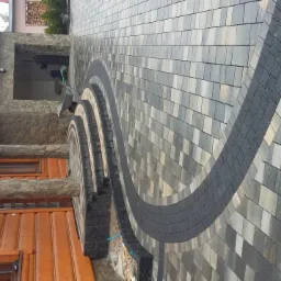 Ułożona kostka brukowa tworząca wzór łuku na posesji z drewnianym domem. Widok z góry, prezentujący estetyczne wykończenie terenu i dopasowanie do architektury.