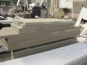 Stos płyt z piaskowca o szorstkiej fakturze, ułożonych na palecie w warsztacie kamieniarskim, z widocznymi śladami obróbki.