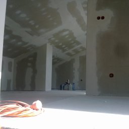 FRB IGMAR Mariusz Igielski - Wnętrze poddasza po montażu płyt kartonowo-gipsowych, widoczne łączenia szpachlowane, przewody elektryczne na ścianie, zwinięty przedłużacz na podłodze w pierwszym planie.