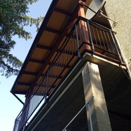 FRB IGMAR Mariusz Igielski - Zadaszony balkon z drewnianym sufitem i metalową balustradą, widok z dołu, z anteną satelitarną na ścianie budynku.