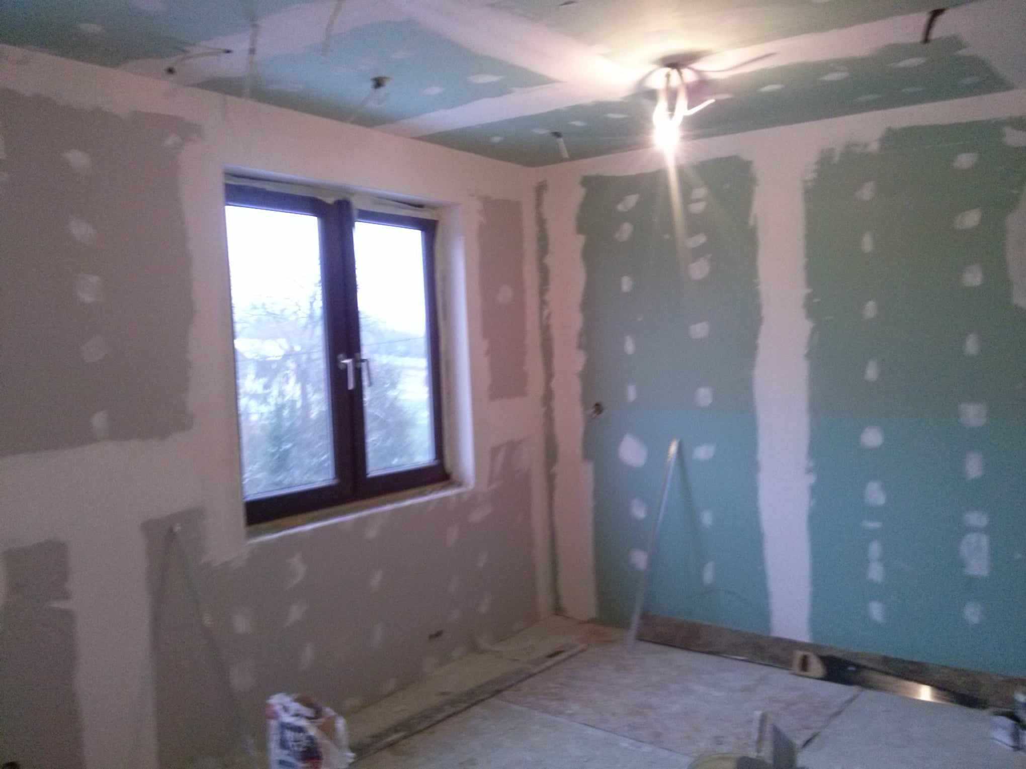 Wnętrze pokoju w trakcie montażu płyt kartonowo-gipsowych na ścianach i suficie, widoczne szpachlowane łączenia i wystające przewody elektryczne.