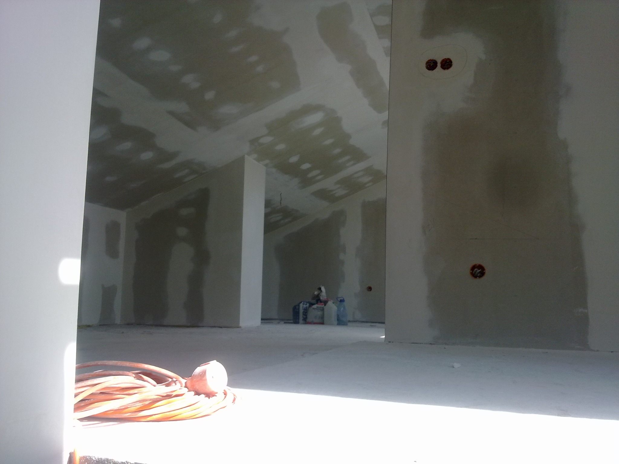 Wnętrze poddasza po montażu płyt kartonowo-gipsowych, widoczne łączenia szpachlowane, przewody elektryczne na ścianie, zwinięty przedłużacz na podłodze w pierwszym planie.