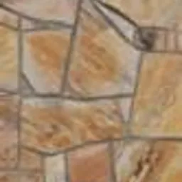 Fragment ściany lub nawierzchni wyłożonej nieregularnymi płytami z gnejsu w odcieniach beżu i brązu, z widocznymi spoinami.