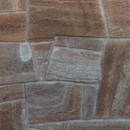 Ściana wyłożona nieregularnymi płytami kamiennymi o zr&oacute;żnicowanej kolorystyce od szarości po rdzawy brąz, połączonymi jasnoszarą fugą. Widoczne naturalne użylenie i tekstura kamienia.