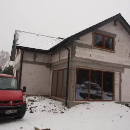 Stan surowy zamknięty domu jednorodzinnego w Otrębusach, widok z zewnątrz w zimowej scenerii, z czerwonym samochodem dostawczym zaparkowanym przed budynkiem.