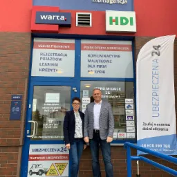 Dwie osoby stojące przed biurem multiagencji ubezpieczeniowej z logo Warta i HDI, na drzwiach informacje o usługach finansowych, rejestracji pojazdów, leasingu, kredytach oraz pełnej ofercie...
