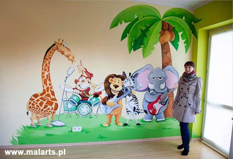 Kobieta w płaszczu stoi na tle ściany z malowidłem przedstawiającym zwierzęta grające w zespole muzycznym: żyrafa, małpa przy perkusji, lew z gitarą, zebra i słoń również z gitarą, a obok palma.