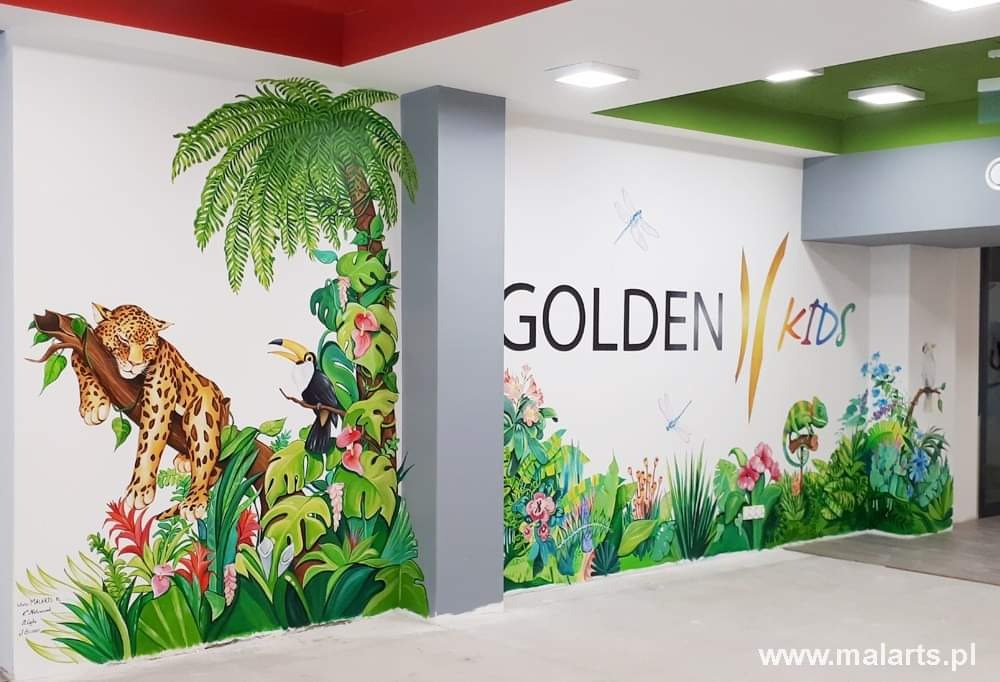 Ściana w pokoju dziecięcym z ręcznie malowanym motywem dżungli, przedstawiającym śpiącego jaguara na drzewie, tukana, tropikalne rośliny oraz napis 'Golden Kids' z motywami roślinnymi i ważkami.