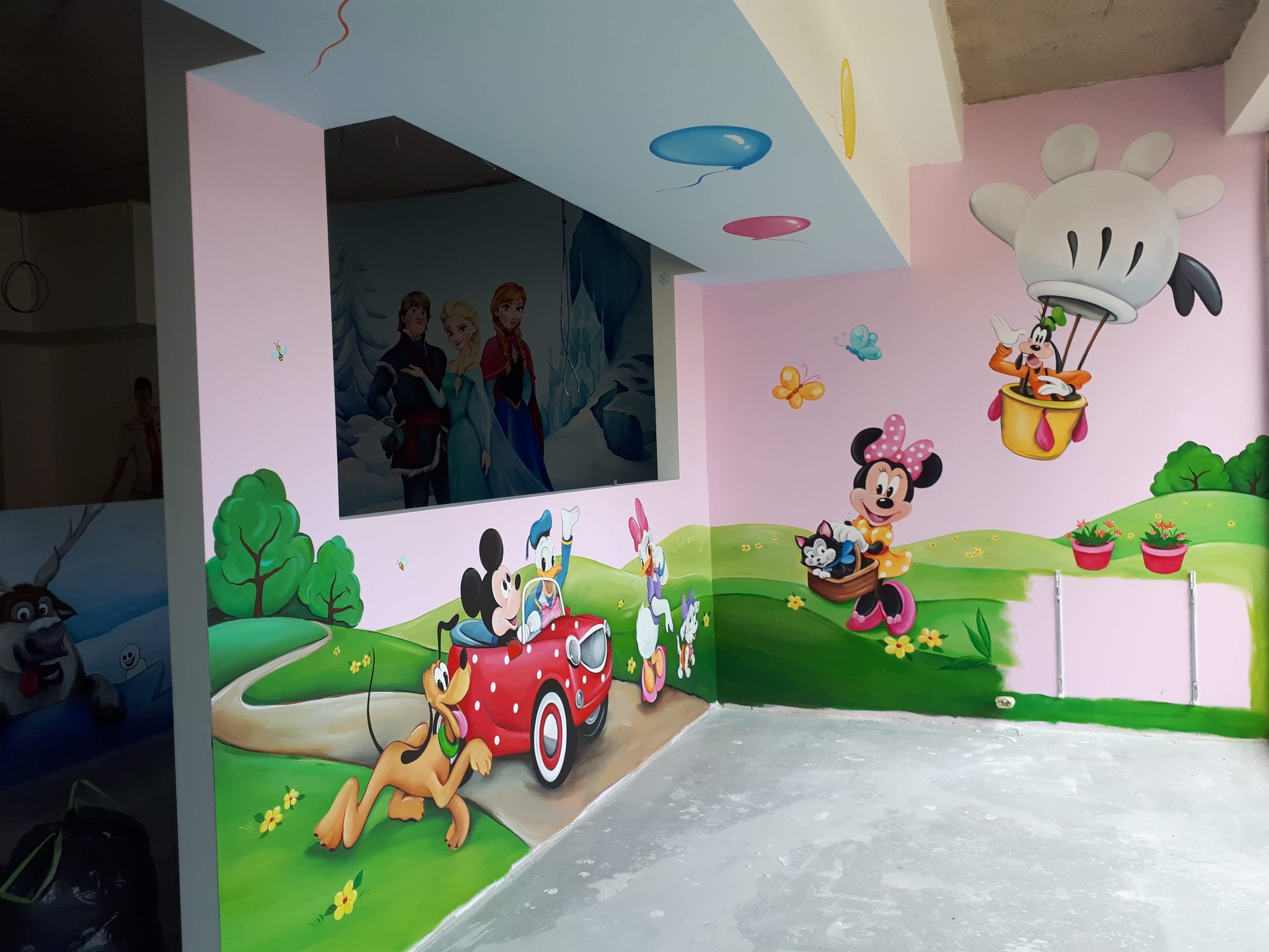 Pokój dziecięcy z ręcznie malowanymi postaciami z bajek Disneya i Krainy Lodu na ścianach, w tym Mickey Mouse w czerwonym samochodzie, Goofy w balonie i Elsa z Anną, z niedokończonym fragmentem...