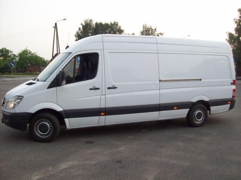 Biały Mercedes Sprinter Maxi z 2006 roku, blaszak, zaparkowany w Zgierzu, widok z boku na tle zieleni i słupów energetycznych.