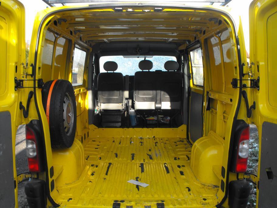 Wnętrze pustego, żółtego busa z otwartymi tylnymi drzwiami. Koło zapasowe zamocowane z boku. Widoczne siedziska kierowcy i pasażera.