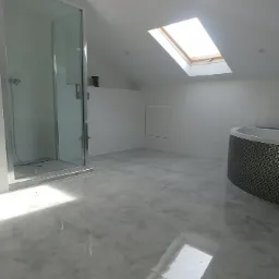 Nowoczesna łazienka na poddaszu z kabiną prysznicową, wanną z mozaiką i oknem dachowym, wykończona w bieli i szarości z błyszczącymi płytkami podłogowymi.