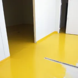 Świeżo wylana, żółta posadzka w pomieszczeniu przemysłowym, z widocznym odpływem liniowym i niedomalowanymi fragmentami przy ścianie.