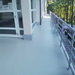 Jasnoszara, gładka powierzchnia tarasu na zewnątrz budynku, z metalową barierką i donicami z fioletowymi kwiatami, widok wzdłuż długiego tarasu.